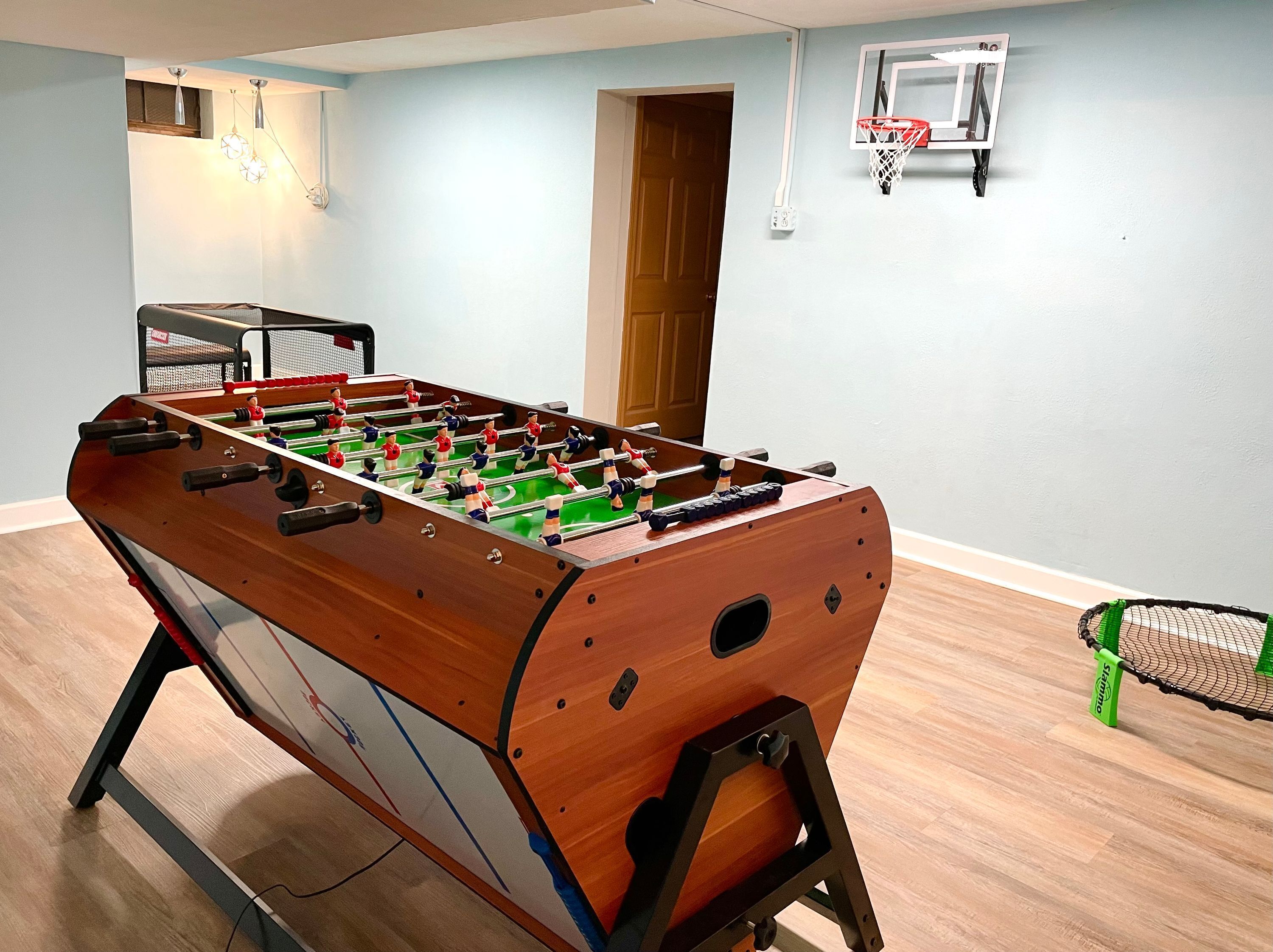 A foosball table in a room with light blue walls, a basketball hoop, and a door.