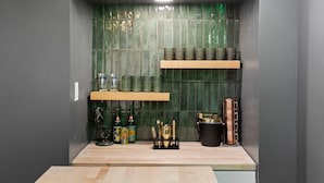 Een compacte keuken met een houten aanrechtblad, een groene betegelde achterwand en planken met keukengerei en flessen.