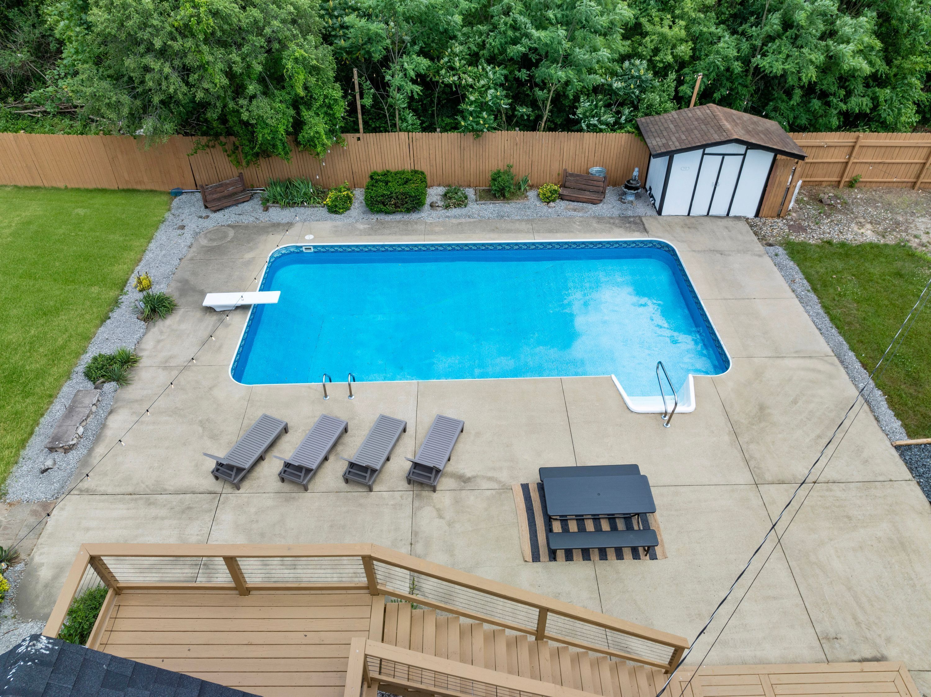 A rectangular swimming pool with a wooden deck surrounding it, equipped with lounge chairs and a small shed.