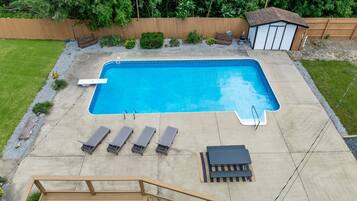 A rectangular swimming pool with a wooden deck surrounding it, equipped with lounge chairs and a small shed.