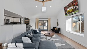 Een moderne woonkamer met een grijze modulaire bank, een houten salontafel en een grote televisie aan de muur.