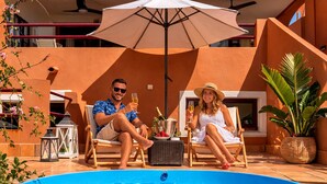 Ein Paar entspannt am Pool mit einem Getränk, umgeben von Gartenmöbeln und Pflanzen.
