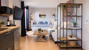 Eine moderne Küche mit Mikrowelle, ein Essbereich mit Holztisch, eine Couch mit gemusterten Kissen und ein Bücherregal mit Dekoration.