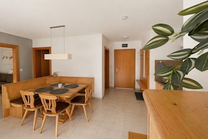 A dining area with a wooden table and chairs, a hanging light fixture, and a door in the background. - Apartment with terrace in Hollersbach (Hollersbach im Pinzgau)