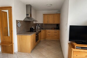 A compact kitchen with wooden cabinets, a stove, and a television on a wooden stand. - Apartment with terrace in Hollersbach (Hollersbach im Pinzgau)