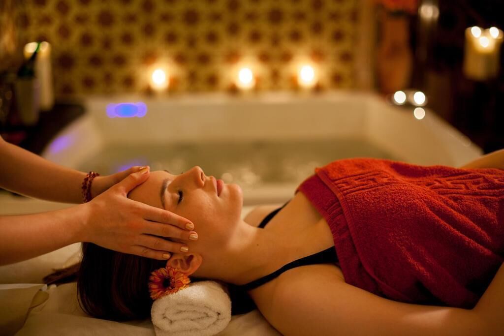 A person receiving a facial treatment in a room with a bathtub and candles in the background.