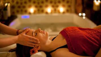 A person receiving a facial treatment in a room with a bathtub and candles in the background.