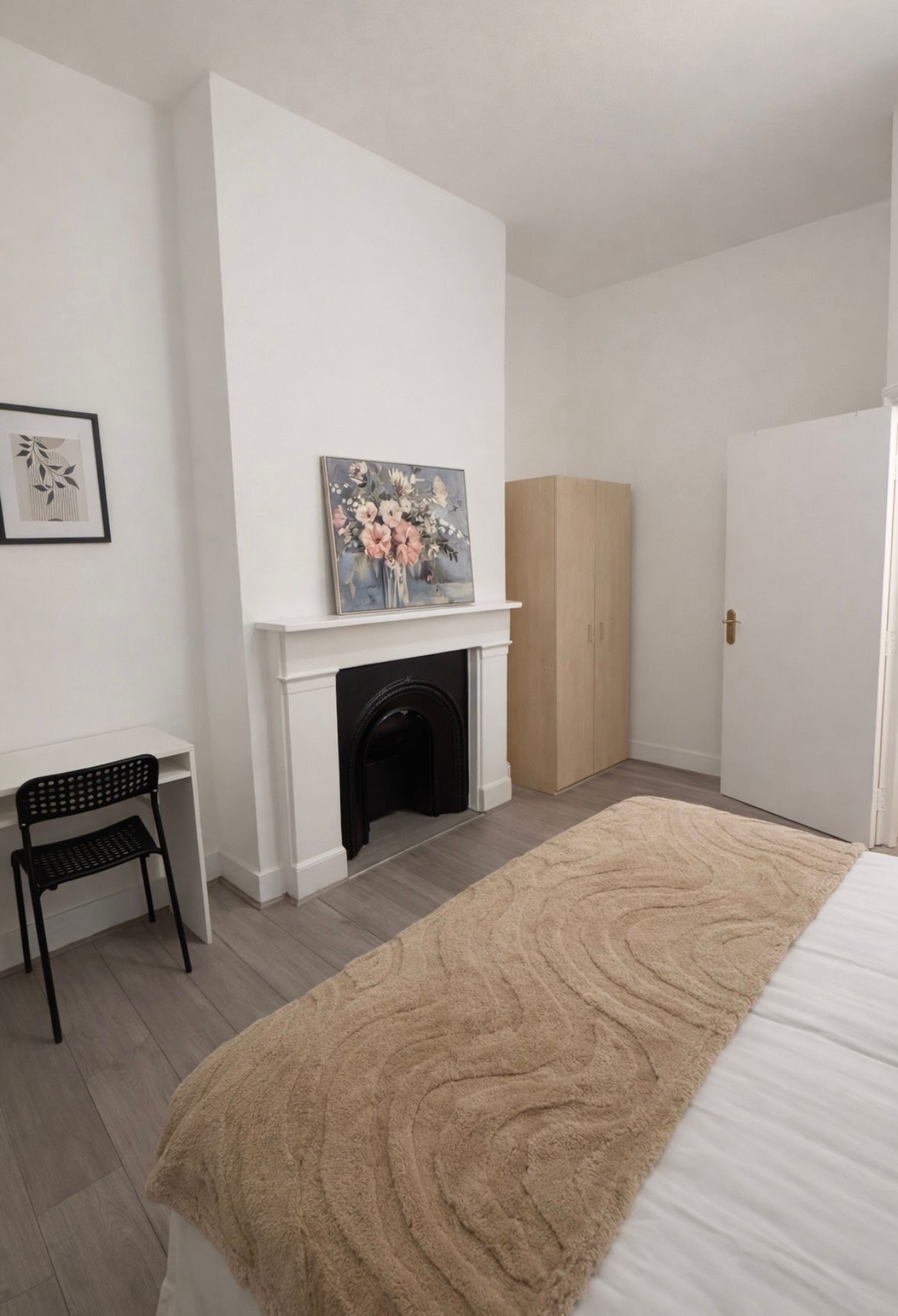Um quarto com cama branca, lareira, uma cadeira preta e um guarda-roupa.