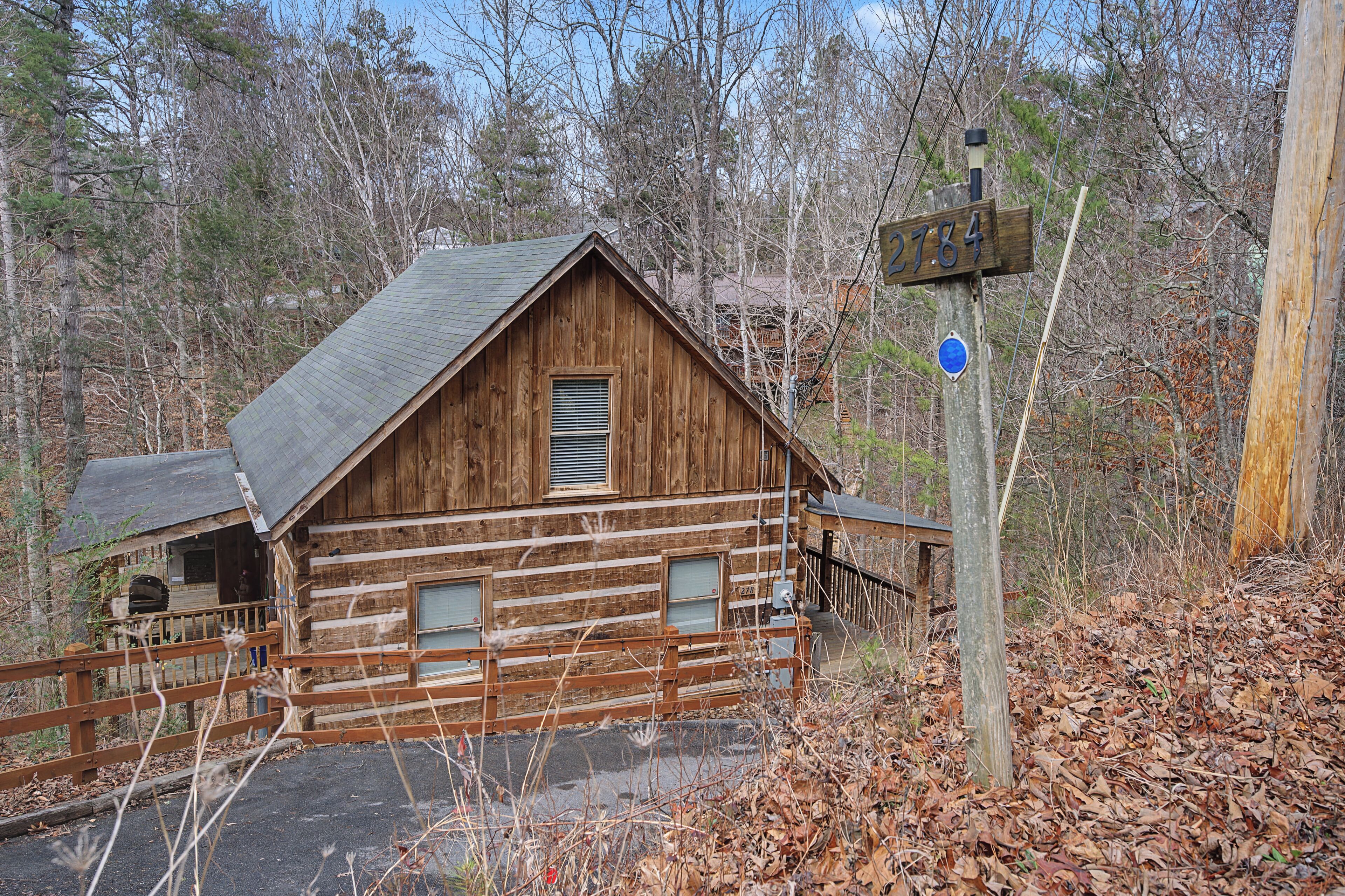 Une cabane en bois rustique, surmontée d’un toit en métal, entourée d’arbres et d’une clôture en bois.