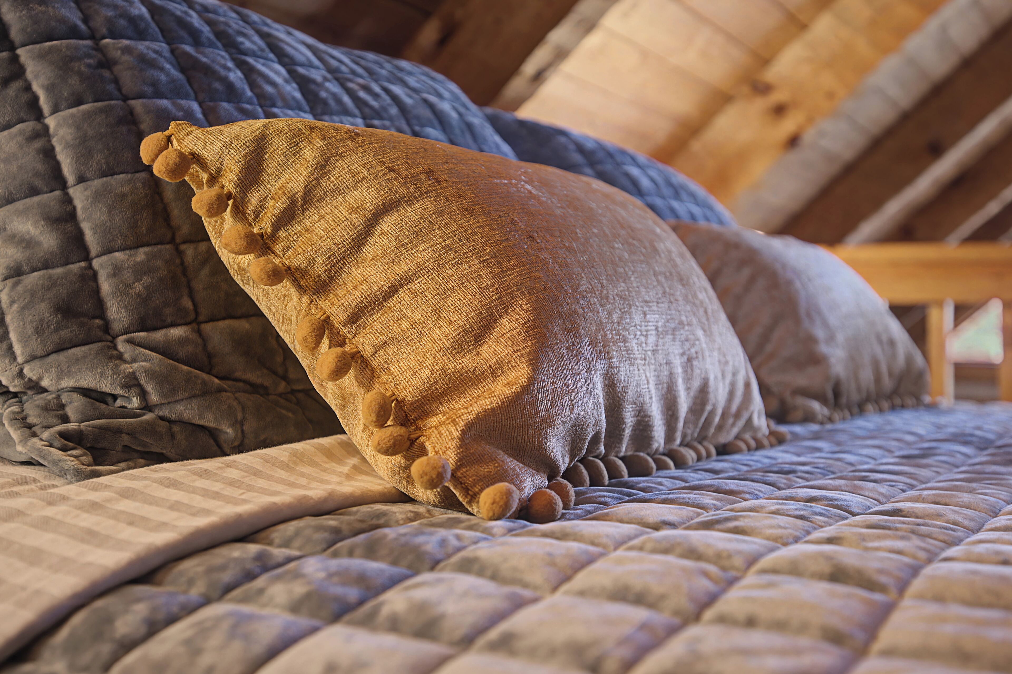 Una cama con cubrecolchón acolchado y dos almohadas, una con flecos.