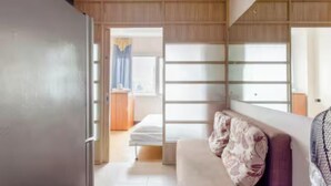 Ein modernes Hotelzimmer mit einer Holzwand, einer Couch mit gemusterten Kissen, einem Bett und einem großen Fenster mit Vorhängen.