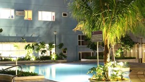 Ein Schwimmbeckenbereich mit einem blauen Gebäude im Hintergrund, umgeben von Palmen und Pflanzen.