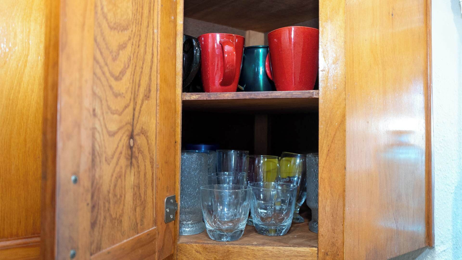 A wooden cabinet with shelves holding various glassware and mugs.
