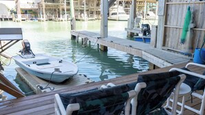 A dock with a boat, wooden deck chairs, and a wooden pier extending into calm water.