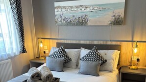Een verzorgde hotelkamer met een groot bed, twee nachtkastjes met lampen, uitzicht op een kustplaats en een mand met handdoeken op het bed.