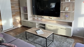 Een moderne woonkamer met een grote flatscreen-televisie, inbouwplanken, een grijze bank en een salontafel.