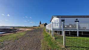 Een gebouw aan de kust met een grindpad dat naar de zee leidt, een omheind gebied en een kerk op de achtergrond.