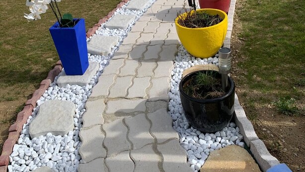 Un chemin de jardin bordé de plantes en pot, avec une voiture garée au fond.
