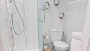 Une salle de bain moderne avec une douche à parois de verre, des toilettes blanches et une petite table ronde dont le piétement est fait d’une structure métallique.