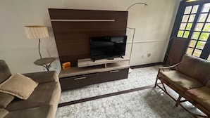 Ett vardagsrum med en TV placerad på ett träskåp, en soffa, en lampa och ett fönster med utsikt.