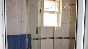 A glass-enclosed shower stall with a towel hanging on the door, a toilet, and a small window above the shower. - Likizo Cottages & Resort Kanamai (Mtwapa)