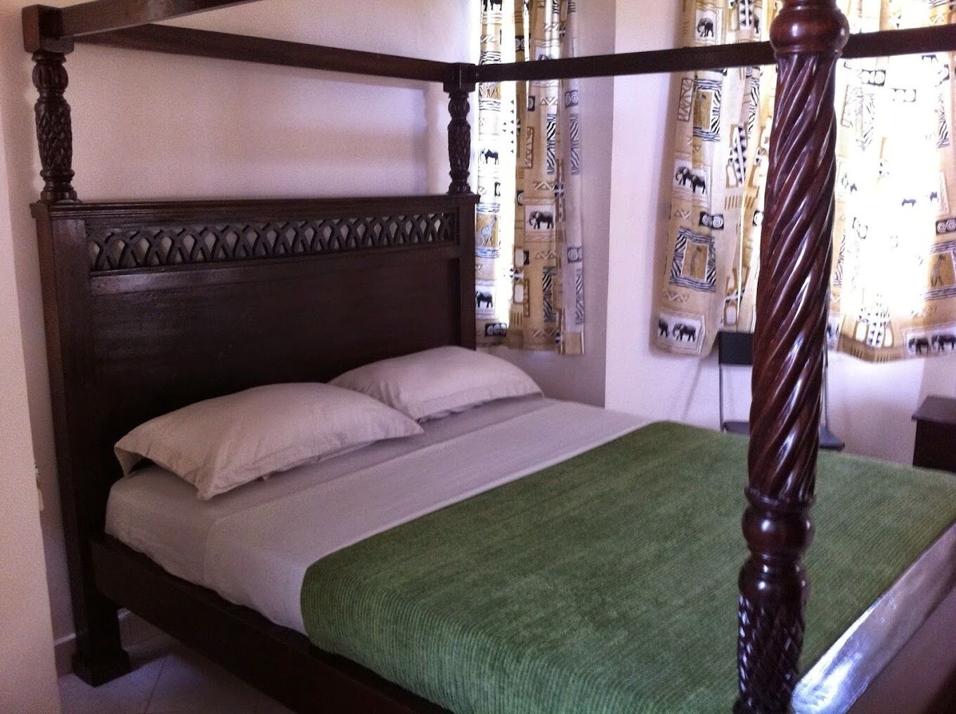 A four-poster bed with a dark wooden headboard and a green throw blanket.