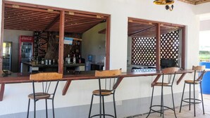 A bar area with wooden bar stools, a Coca-Cola refrigerator, and a wooden ceiling. - Likizo Cottages & Resort Kanamai (Mtwapa)