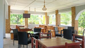 An outdoor restaurant with wooden tables and chairs, stone pillars, and a TV screen. - Likizo Cottages & Resort Kanamai (Mtwapa)