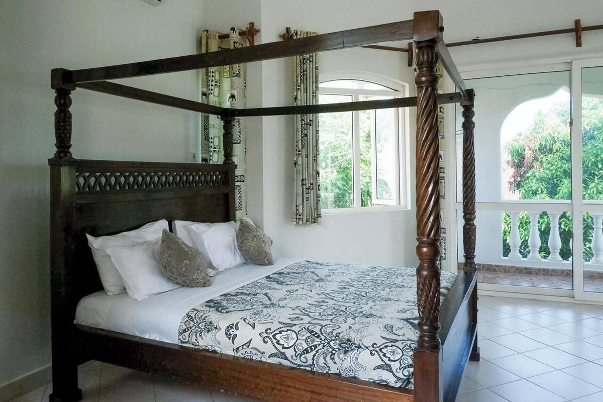 A four-poster bed with a patterned bedspread, a wooden headboard, and a balcony with a railing.