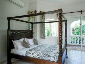 A four-poster bed with a patterned bedspread, a wooden headboard, and a balcony with a railing. - Likizo Cottages & Resort Kanamai (Mtwapa)