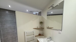 Une salle de bain moderne avec un meuble-lavabo en bois, un lavabo blanc et un miroir au-dessus. On y trouve également un porte-serviettes et une petite étagère avec une plante.