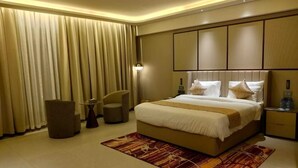 Una habitación de hotel moderna con una cama grande, una mesita de noche, una silla y un ventanal con cortinas.