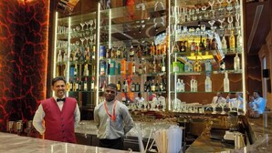 Una zona de bar con estanterías llenas de botellas de licor y vasos.