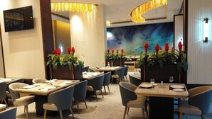 Un comedor moderno con mesas rectangulares, sillas azules y plantas decorativas con flores rojas.