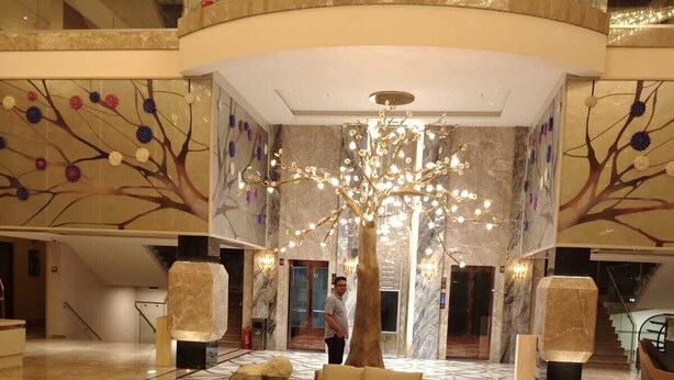 Un vestíbulo amplio con un sofá curvo, un árbol decorativo en el centro y un candelabro.