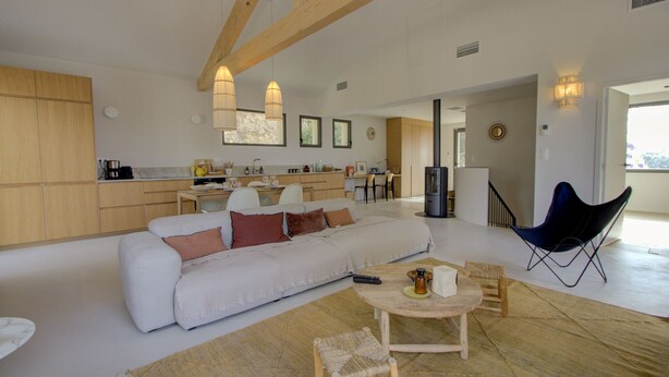 Uma sala ampla com sofá, mesa de centro e cadeiras, uma cozinha com armários de madeira e uma área de jantar com mesa e cadeiras.