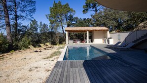 Piscina com espreguiçadeiras, varanda coberta e vista para árvores.