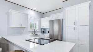 Une cuisine moderne avec des meubles blancs, un réfrigérateur en acier inoxydable et un îlot central doté d’une plaque de cuisson intégrée.