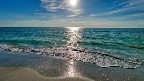 Une plage avec un ciel dégagé et la lumière du soleil se reflétant sur l’eau.