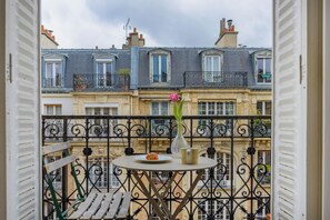 A balcony with a round table, a vase with flowers, and a croissant on a plate. - Paris sacré coeur prestige residence (Paris)