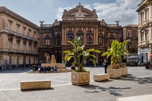 Ein historisches Gebäude mit aufwendiger Architektur, einer zentralen Fontäne und Sitzbereichen mit Pflanzenkübeln.