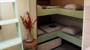 Pieni huone, jossa on kerrossängyt, pieni jakkara, patteri ja ikkuna.