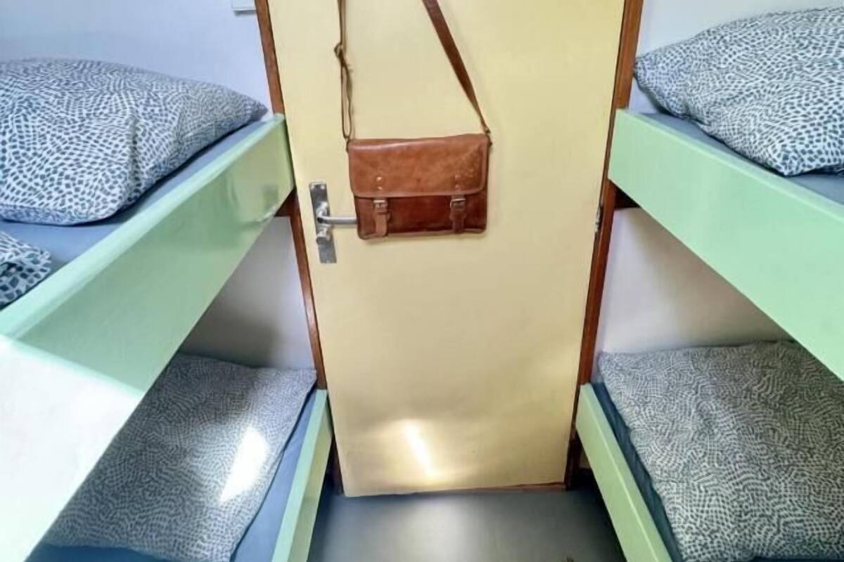 A room with bunk beds, a door with a hat and bag hanging on it, and a small wooden stool.