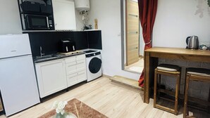 Uma cozinha moderna com armários brancos, micro-ondas, máquina de lavar e um espaço de refeições com uma mesa pequena e banquetas.