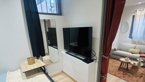 Quarto de hotel com cama, televisão, secretária, espelho e vista exterior.