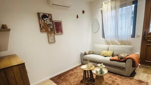 Uma sala de estar com um sofá cinzento, um tapete castanho e um armário de madeira.