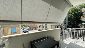 An outdoor seating area with a table and chairs, a covered section, and a view of the street with parked cars and buildings. - Beachfront with ⛱️ umbrella included (Pescara)