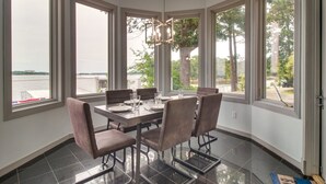 A dining area with a table set for four, large windows with a view of a body of water, and a modern chandelier.