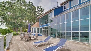 A wooden deck with lounge chairs and a table, overlooking a large glass building with a blue exterior.