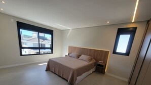 Une chambre moderne avec un grand lit, une table de chevet, un téléviseur fixé au mur et une fenêtre donnant sur des immeubles.